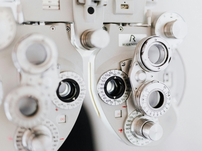 Close-up of a phoropter, an optical device with multiple dials and lenses used by eye care professionals to measure vision and determine eyeglass prescriptions.